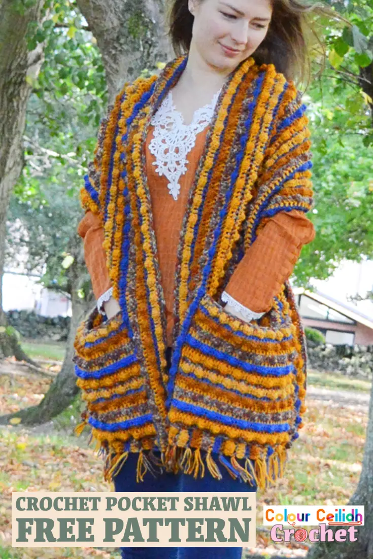 This crochet pocket shawl is called Autumn Berries and it is an easy breezy pattern with the tassel fringe made using the yarn tails from the color change. Featuring a generous size and a simple repeat of 5 colors, this relaxed style shawl is beginner friendly and is great for romantic walks in nature to snuggle yourself into. #crochetpocketshawl #crochet #pocketshawl