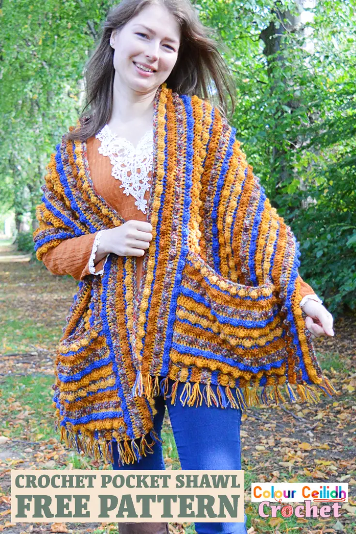 This crochet pocket shawl is called Autumn Berries and it is an easy breezy pattern with the tassel fringe made using the yarn tails from the color change. Featuring a generous size and a simple repeat of 5 colors, this relaxed style shawl is beginner friendly and is great for romantic walks in nature to snuggle yourself into. #crochetpocketshawl #crochet #pocketshawl
