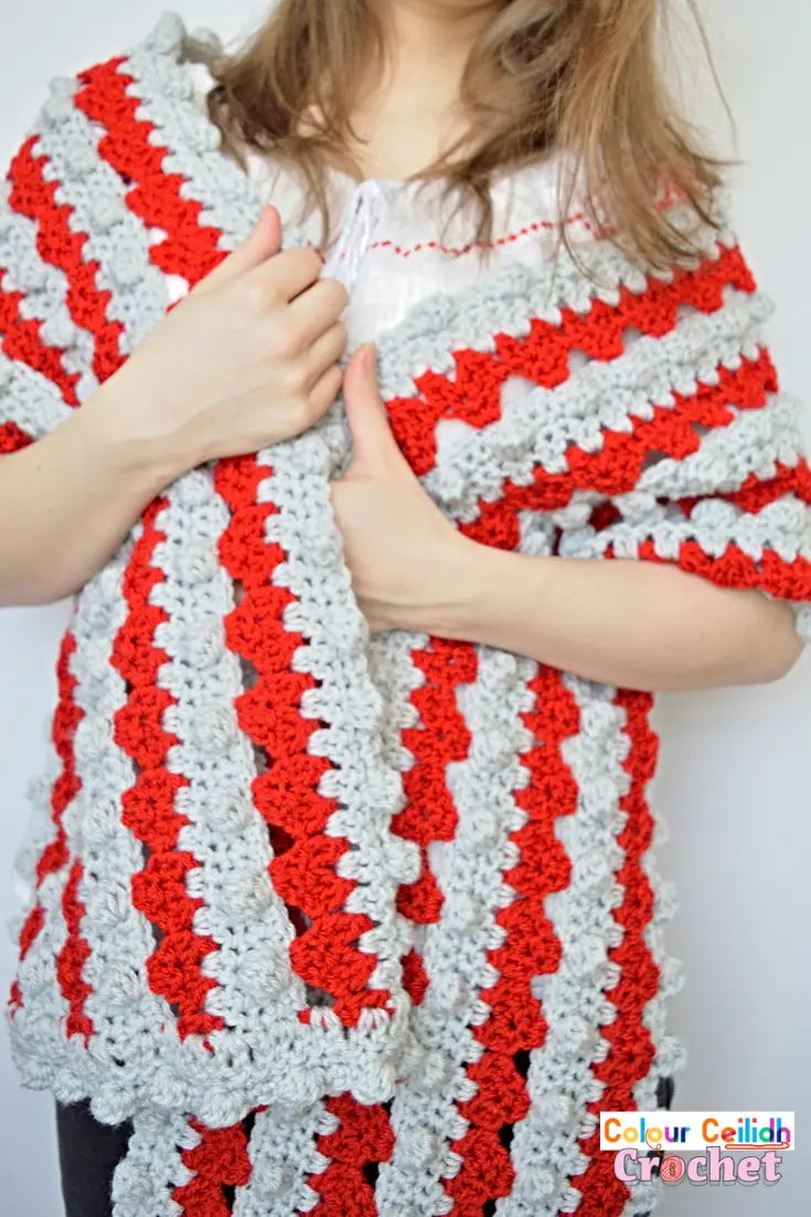 This free and easy crochet heart shawl pattern works crochet hearts in stripes, alternating with rows of crochet bobbles. The crochet heart stitch uses the granny stitch as the base. Together with the large hook size and the larger weight yarn, this makes for a fun and fast Valentine's Day project that you can wrap around your shoulders. Includes a video tutorial.